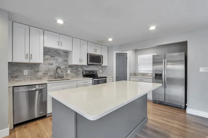 Kitchen featuring stainless steel appliances, light wood-type flooring, a kitchen island, light stone counters, and recessed lighting