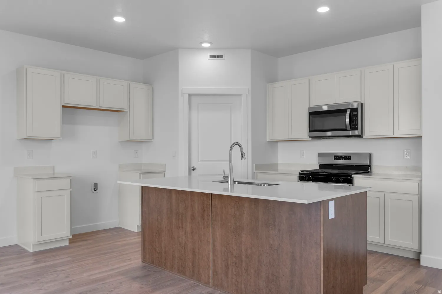 Kitchen featuring an island with sink, stainless steel appliances, dark wood-style flooring, recessed lighting, and light stone counters
