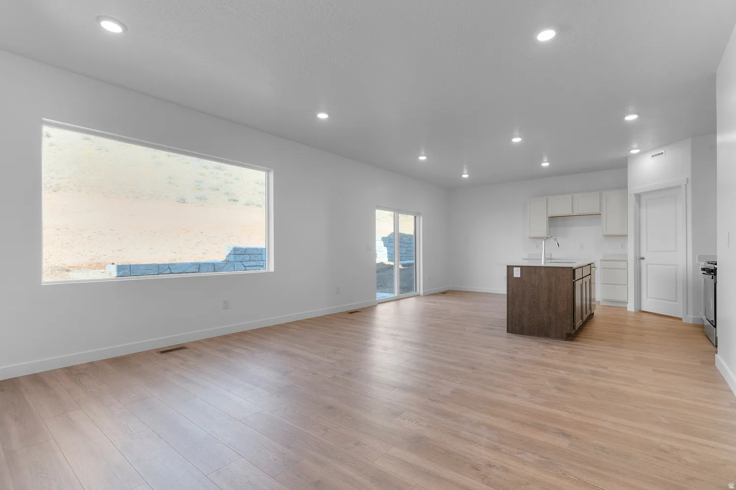 Dual tone kitchen with open floor plan, a kitchen island with sink, light wood finished floors, two tone cabinetry, and recessed lighting