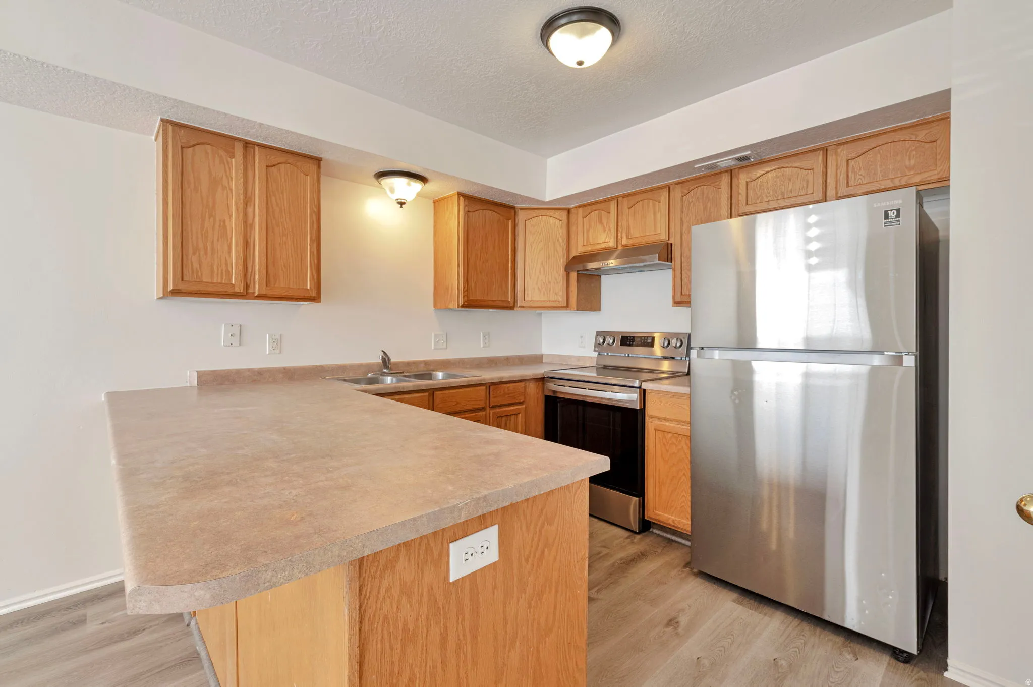 Kitchen featuring stainless steel appliances, a peninsula, light countertops, light wood-style floors, and a textured ceiling