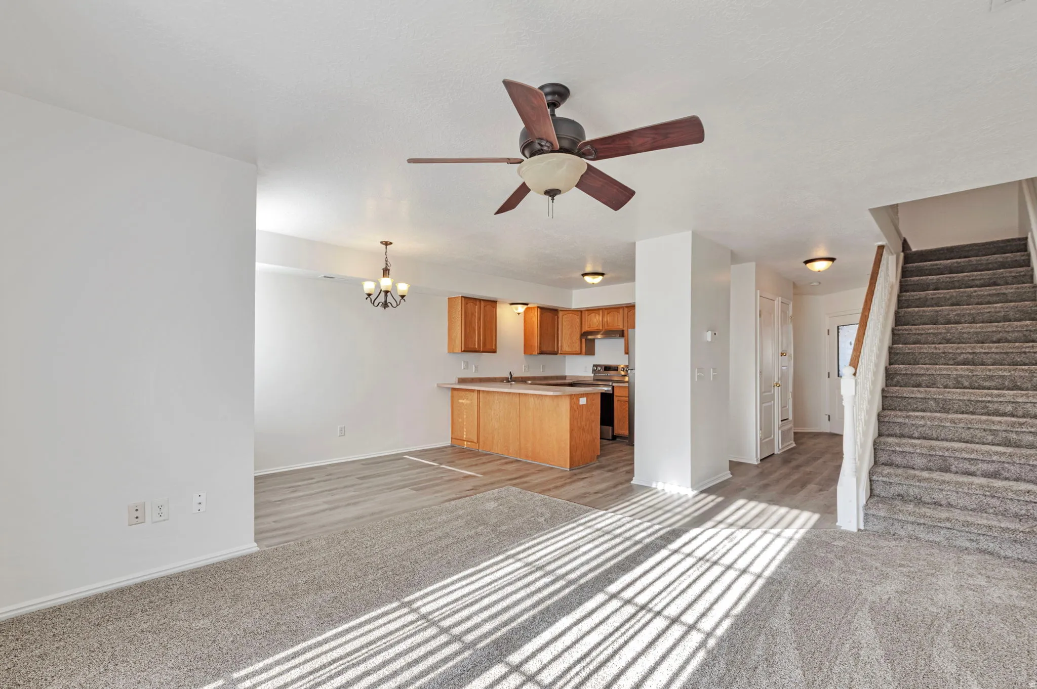 Unfurnished living room featuring light colored carpet, suspended lighting, and a ceiling fan