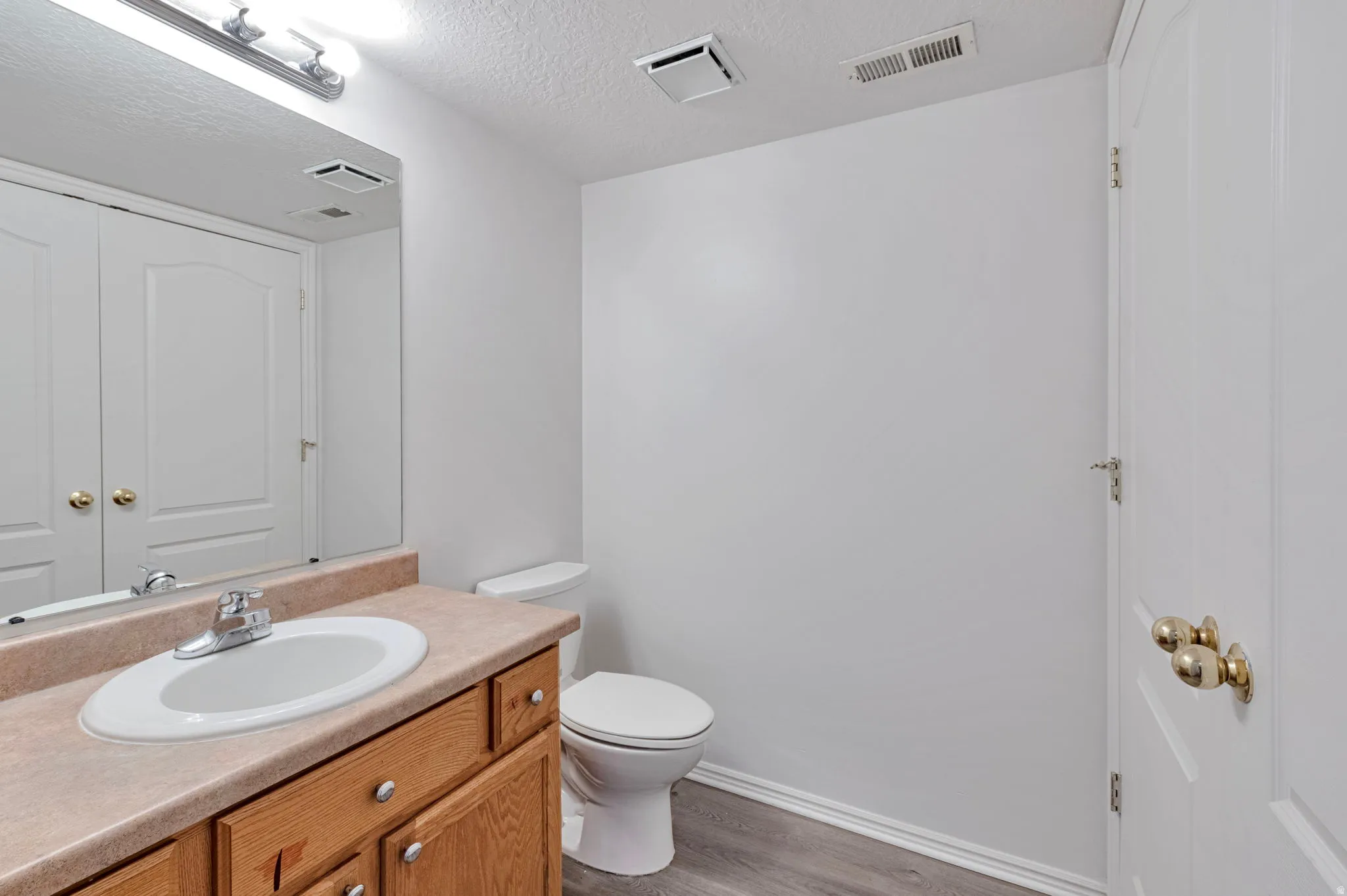 Half bathroom with vanity, light wood-style flooring, and a textured ceiling