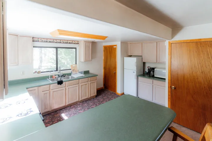 Kitchen featuring light wood finish cabinetry, white appliances, dark flooring, and dark countertops