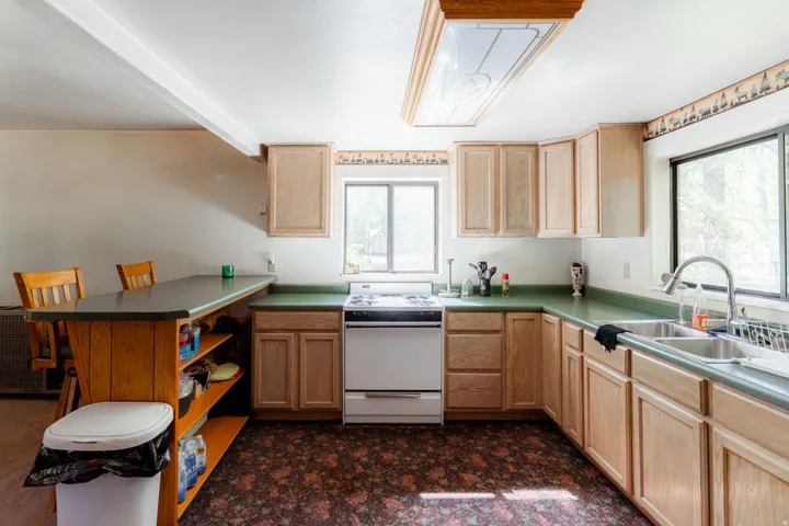 Kitchen featuring a peninsula, white range with gas stovetop, light wood finish cabinets, open shelves, and beamed ceiling