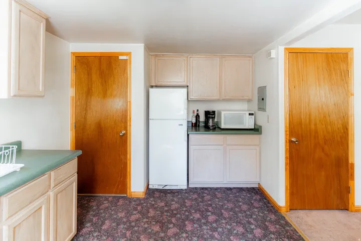 Kitchen with light wood finish cabinets, white appliances, and dark countertops