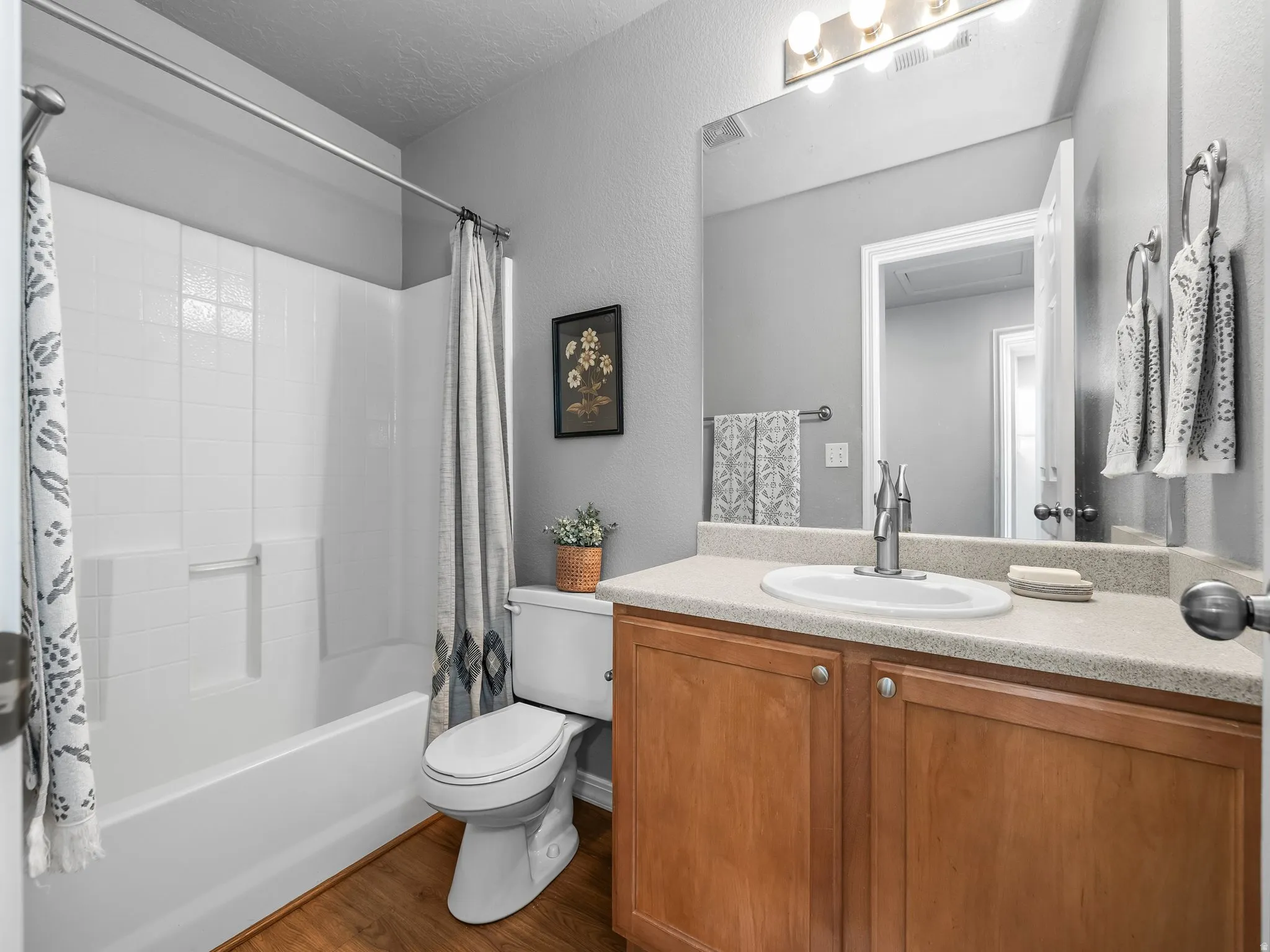 Full bath with vanity, a textured wall, shower / tub combo, dark wood-style flooring, and a textured ceiling