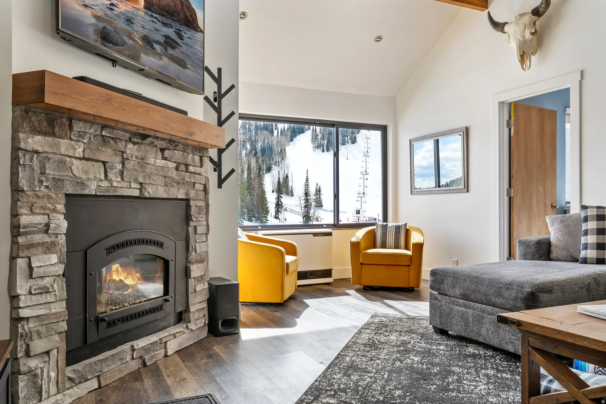 Living room featuring wood finished floors, a stone fireplace, and lofted ceiling with beams