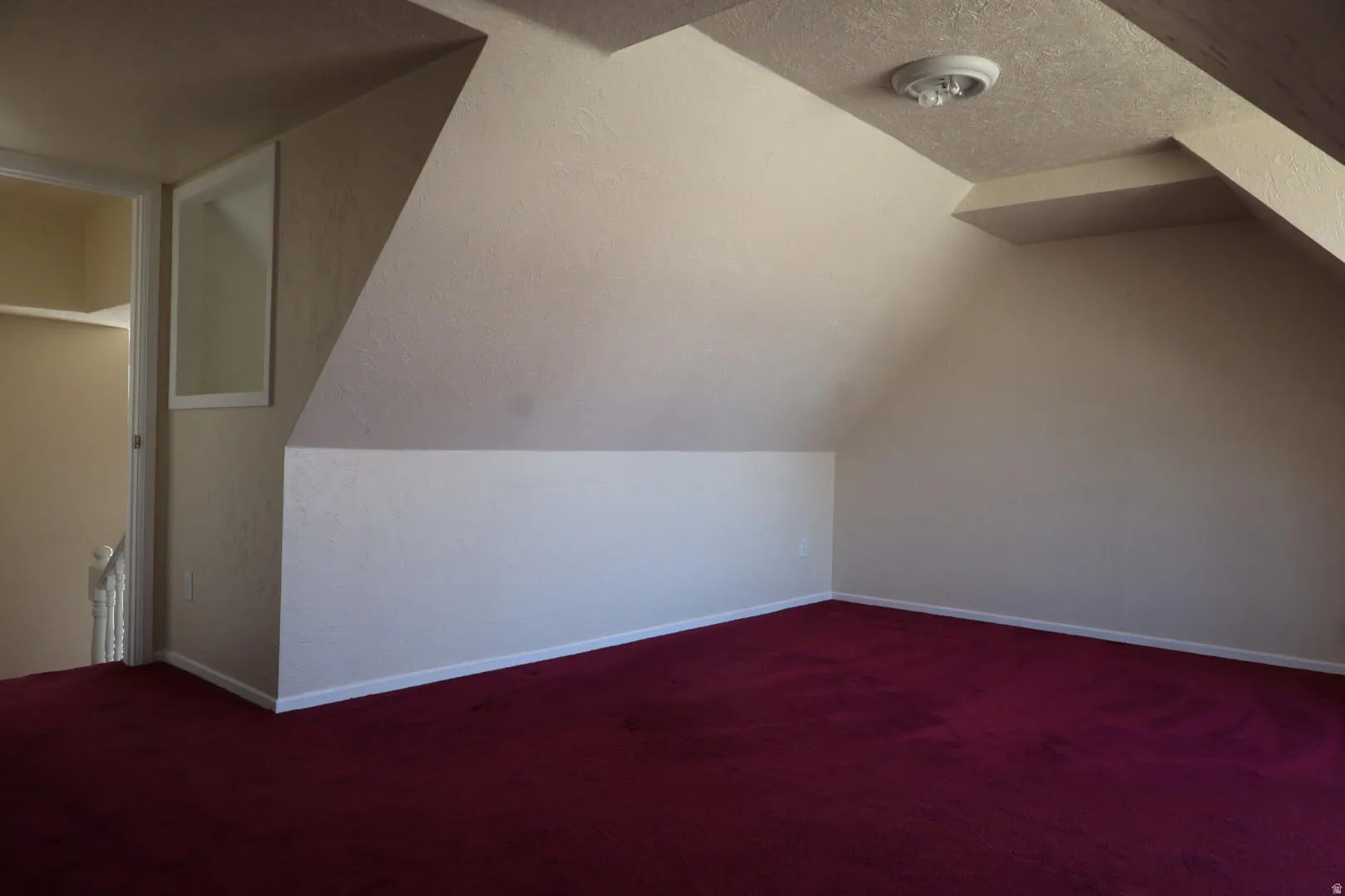 Bonus room featuring dark carpet and baseboards