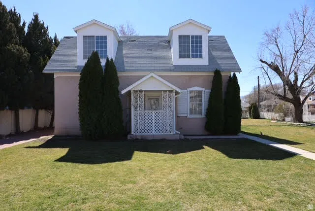 Cape cod house with a front yard, stucco siding, and covered porch