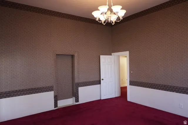 Empty room featuring a chandelier, dark colored carpet, wallpapered walls, and a high ceiling