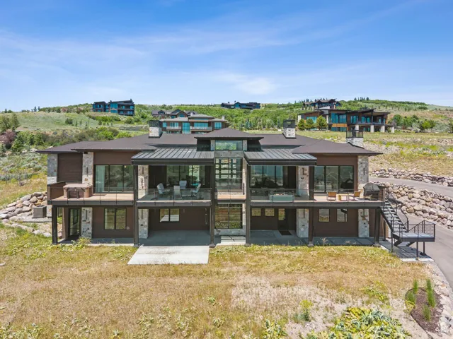Rear view of house with a standing seam roof, stone siding, a patio area, and a balcony