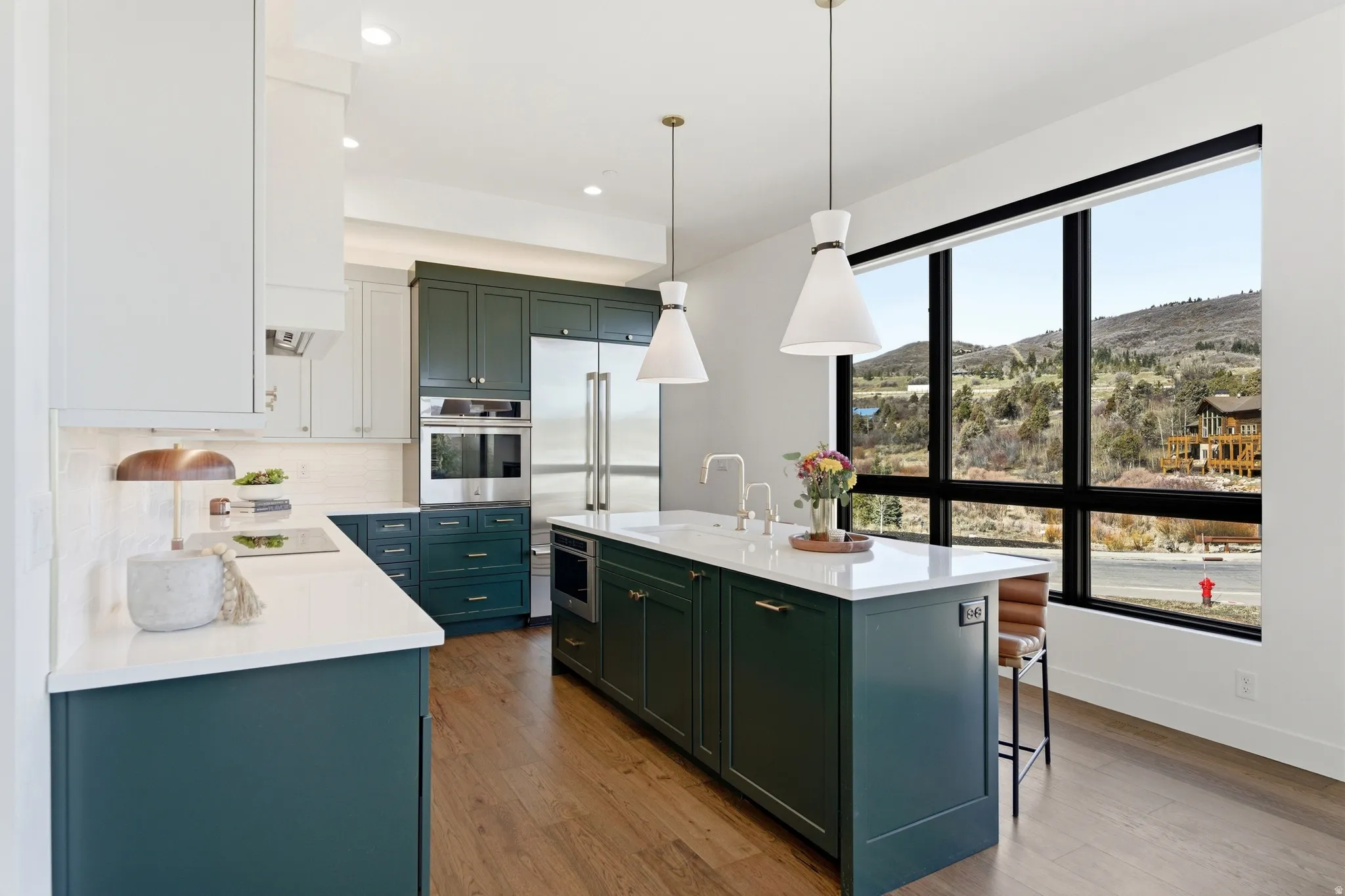 Kitchen featuring an island with sink, stainless steel appliances, light stone countertops, a mountain view, and light wood-style flooring
