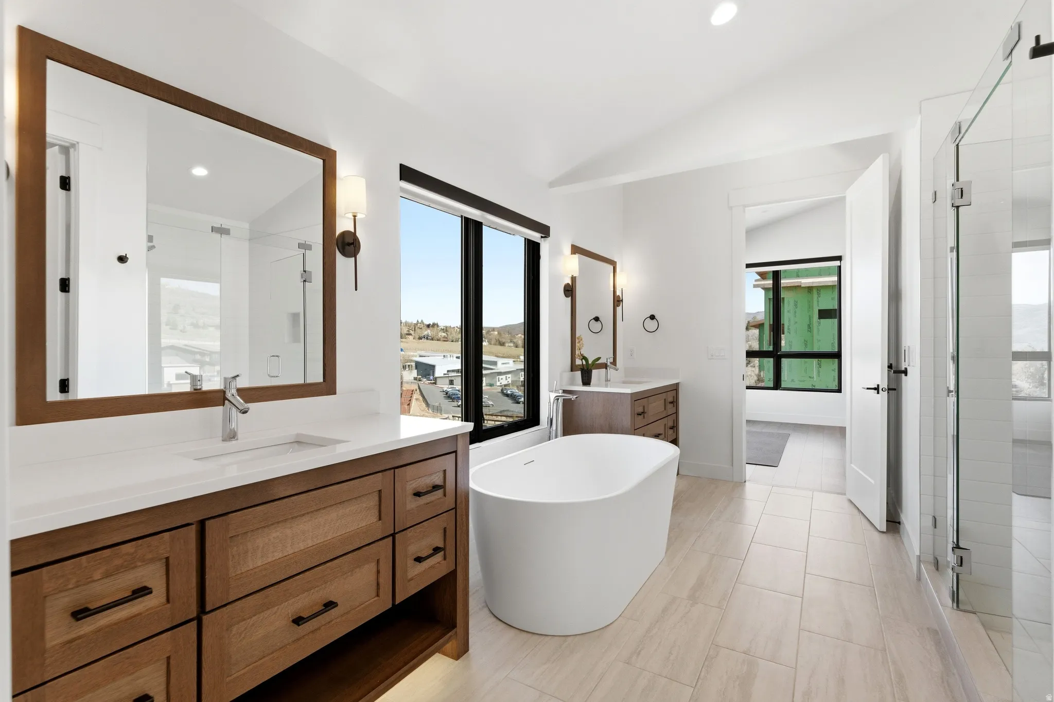 Full bathroom featuring a shower stall, two vanities, a freestanding tub, vaulted ceiling, and recessed lighting