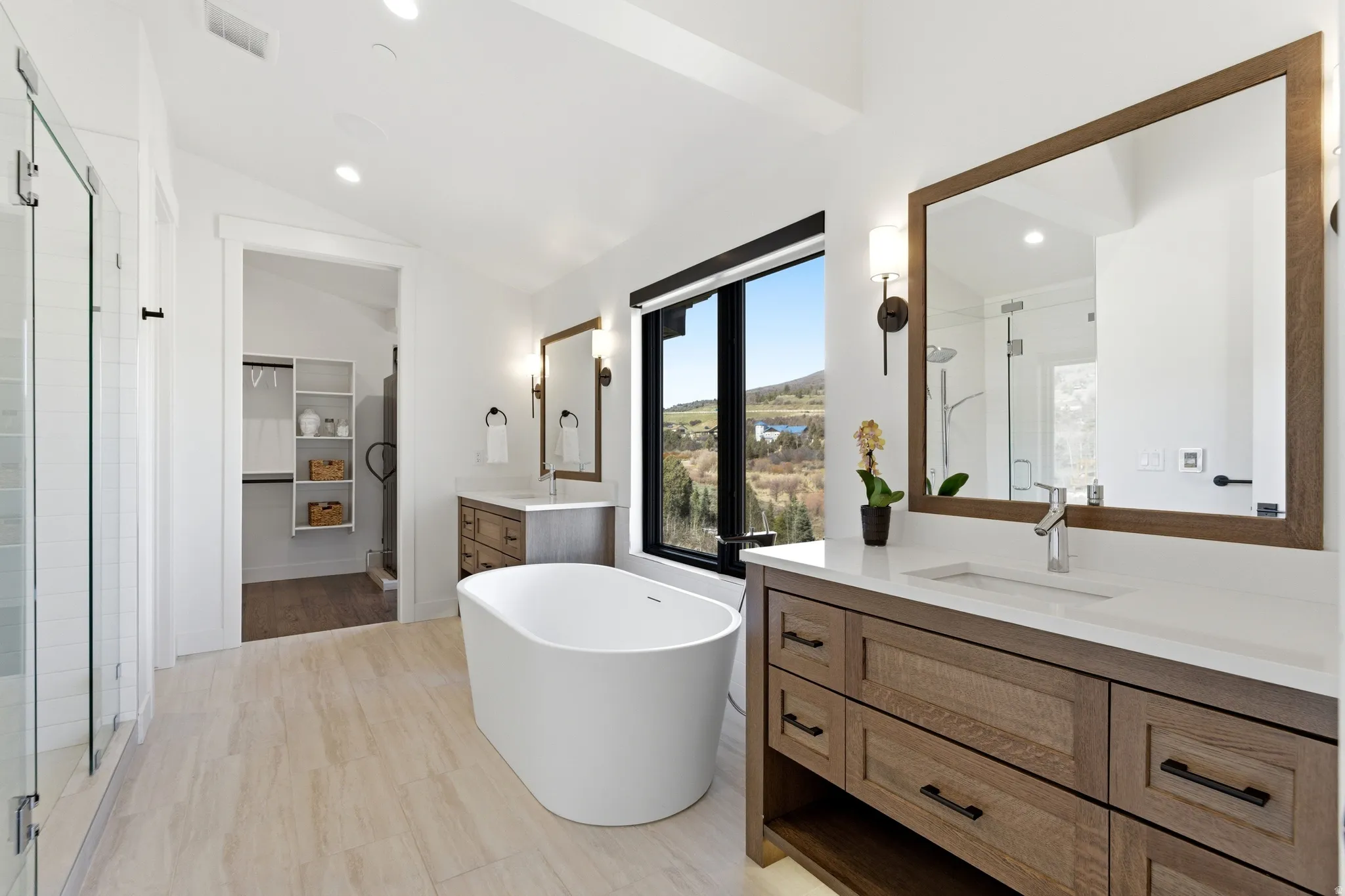 Bathroom with a stall shower, two vanities, a freestanding bath, recessed lighting, and vaulted ceiling