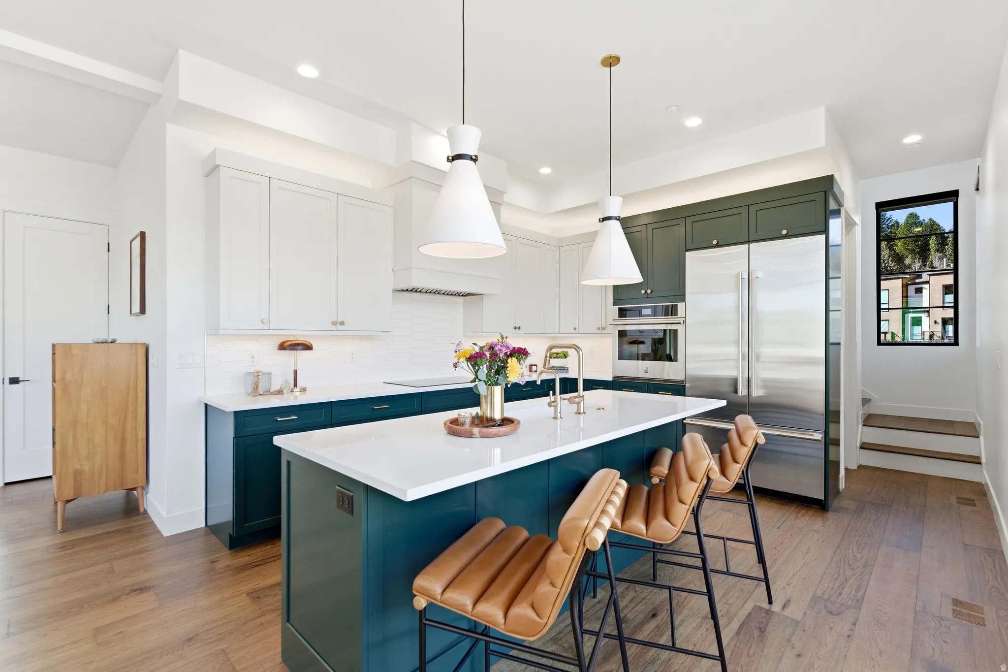 Kitchen with dual tone cabinets, dark wood-type flooring, stainless steel appliances, a kitchen bar, and a center island with sink