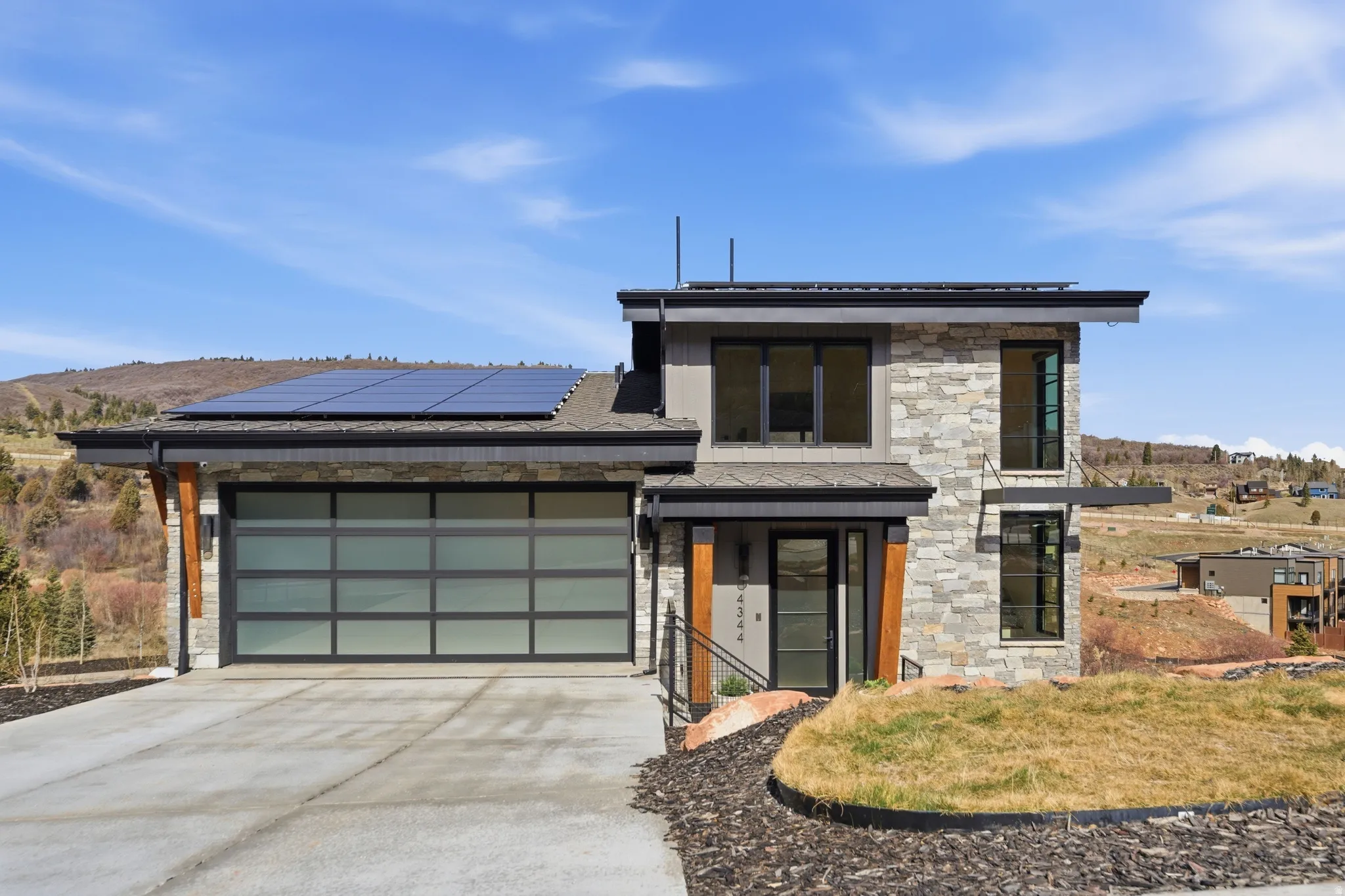 Contemporary house with stone siding, solar panels, concrete driveway, an attached garage, and a mountain view