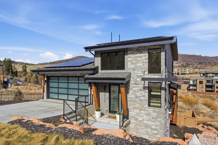 Modern home featuring roof mounted solar panels, concrete driveway, stone siding, a mountain view, and a garage