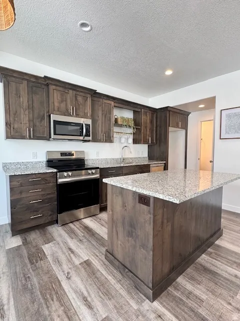Kitchen featuring dark wood finish cabinets, stainless steel appliances, open shelves, light stone countertops, and a textured ceiling
