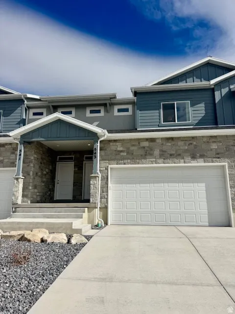 View of front of house featuring stone siding, driveway, an attached garage, and board and batten siding