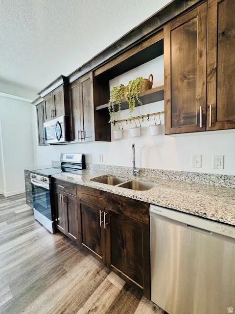 Kitchen with stainless steel appliances, open shelves, dark wood finish cabinetry, light stone countertops, and a textured ceiling