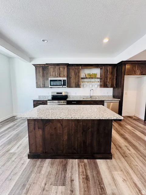 Kitchen featuring dark wood finish cabinetry, a center island, open shelves, stainless steel appliances, and light wood finished floors