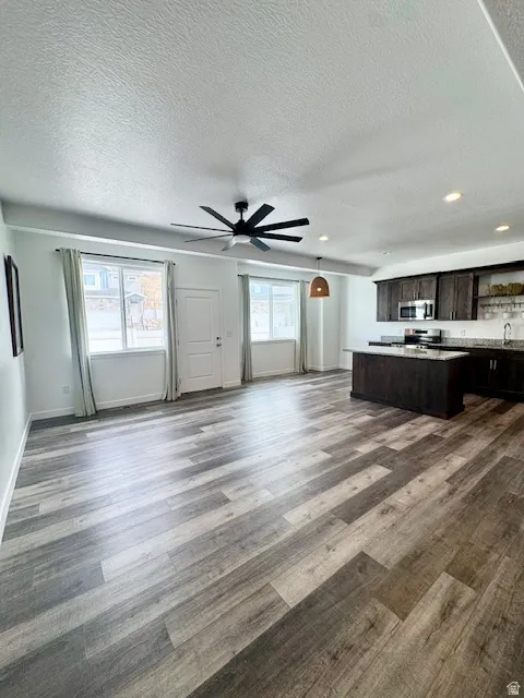 Kitchen featuring dark wood finish cabinets, open floor plan, a center island, a textured ceiling, and stainless steel appliances