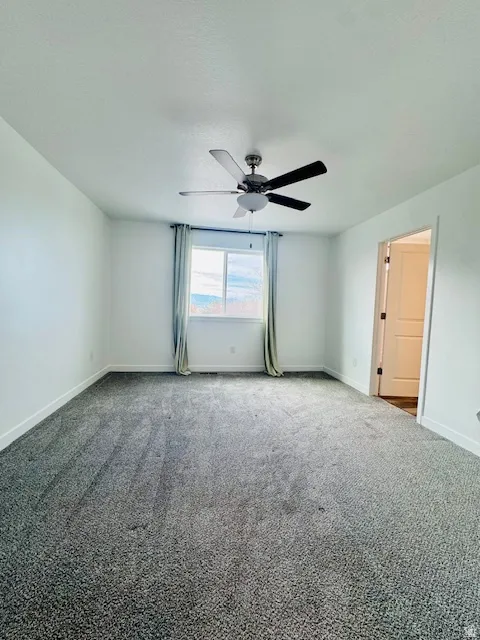 Carpeted empty room with baseboards and a ceiling fan
