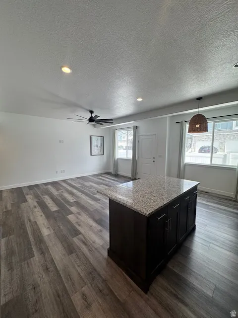 Kitchen featuring a center island, light stone countertops, dark wood-type flooring, hanging light fixtures, and ceiling fan
