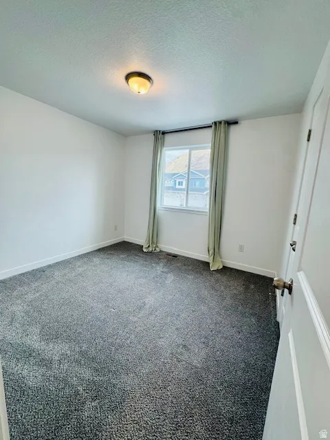 Empty room featuring a textured ceiling and dark carpet