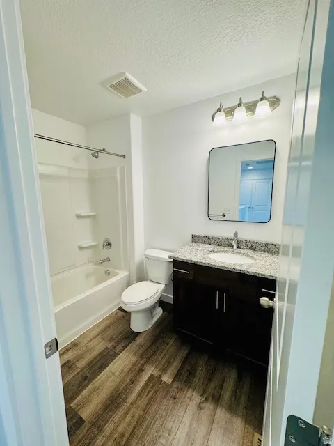 Full bathroom featuring vanity, dark wood-style floors, a textured ceiling, and  shower combination
