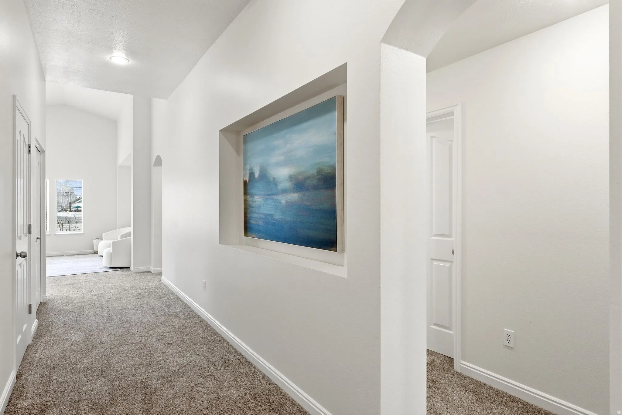 Corridor featuring light colored carpet, lofted ceiling, and arched walkways