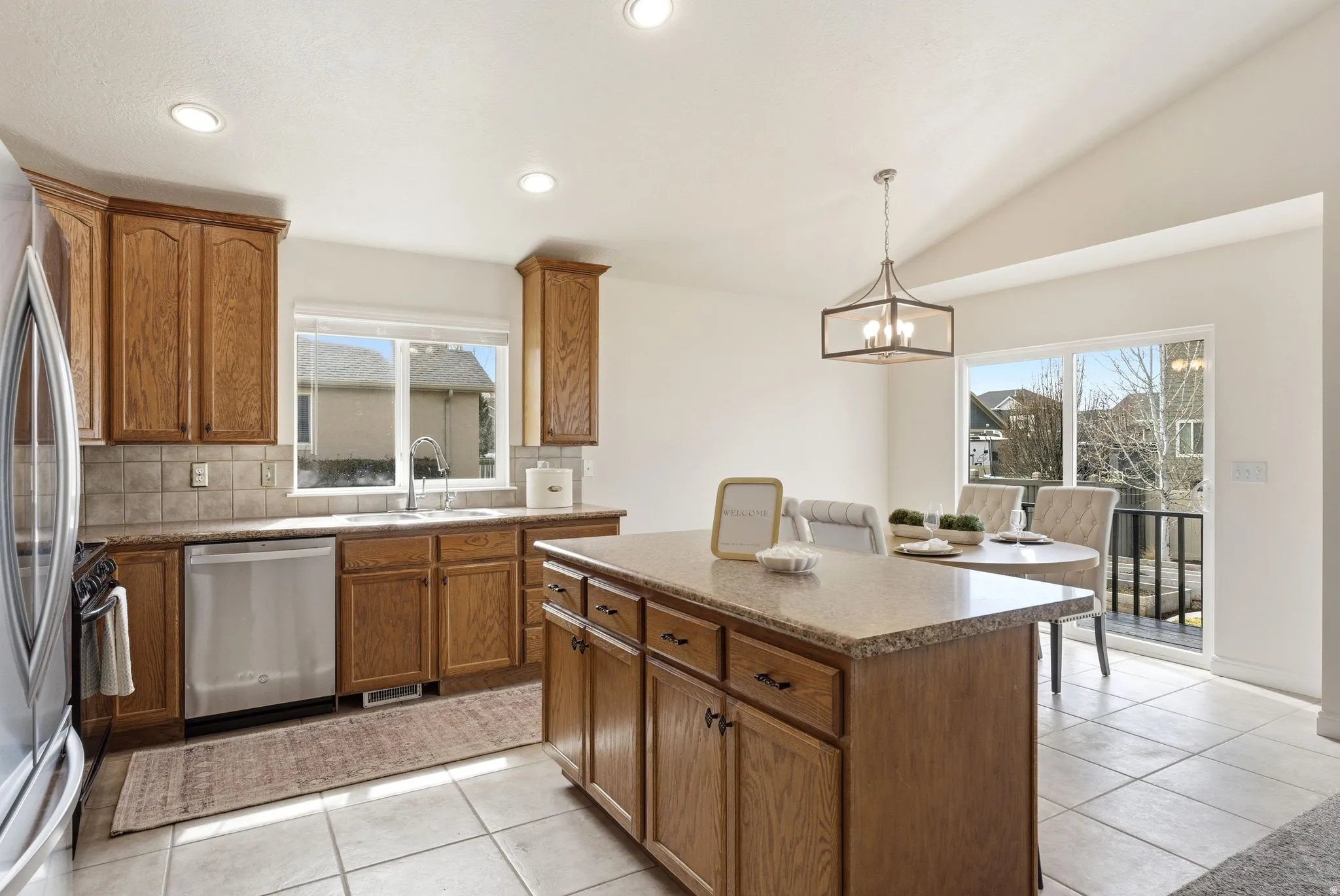 Kitchen with wood finish cabinetry, a center island, stainless steel appliances, light tile patterned floors, and vaulted ceiling