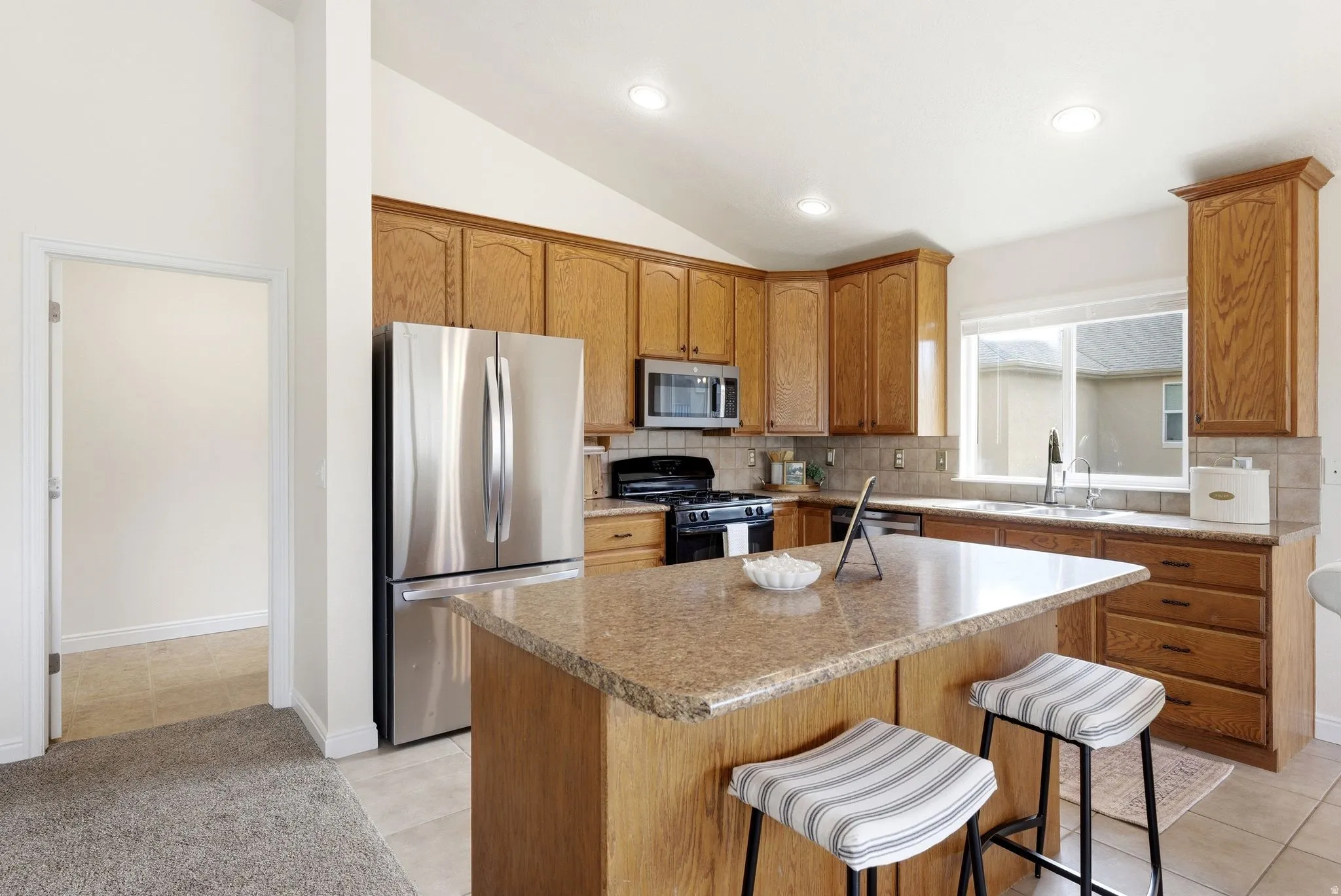 Kitchen featuring stainless steel appliances, tasteful backsplash, a breakfast bar, wood finish cabinetry, and light countertops