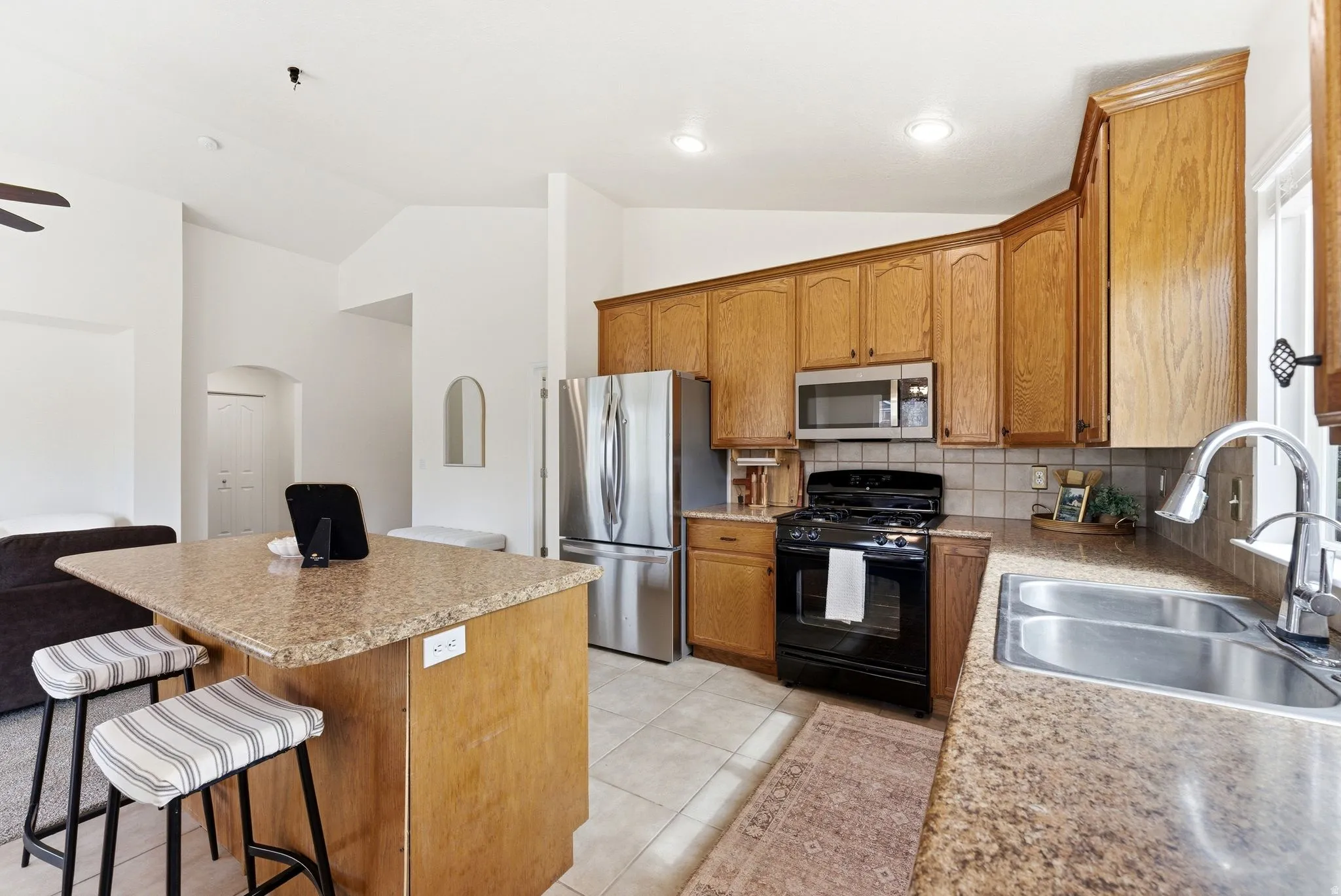 Kitchen with arched walkways, stainless steel appliances, a center island, tasteful backsplash, and lofted ceiling