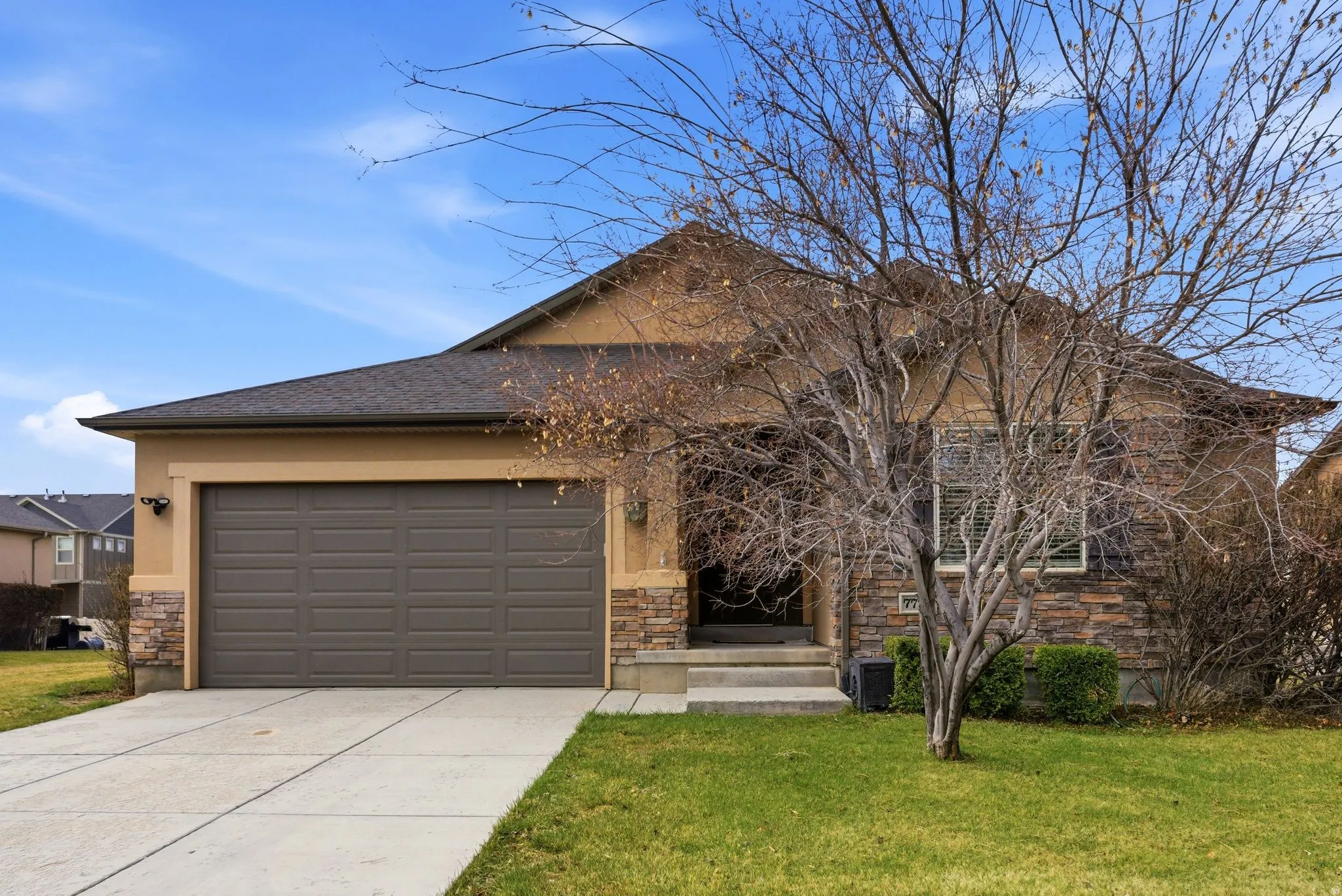 View of front of house featuring stone siding, driveway, a front yard, and an attached garage