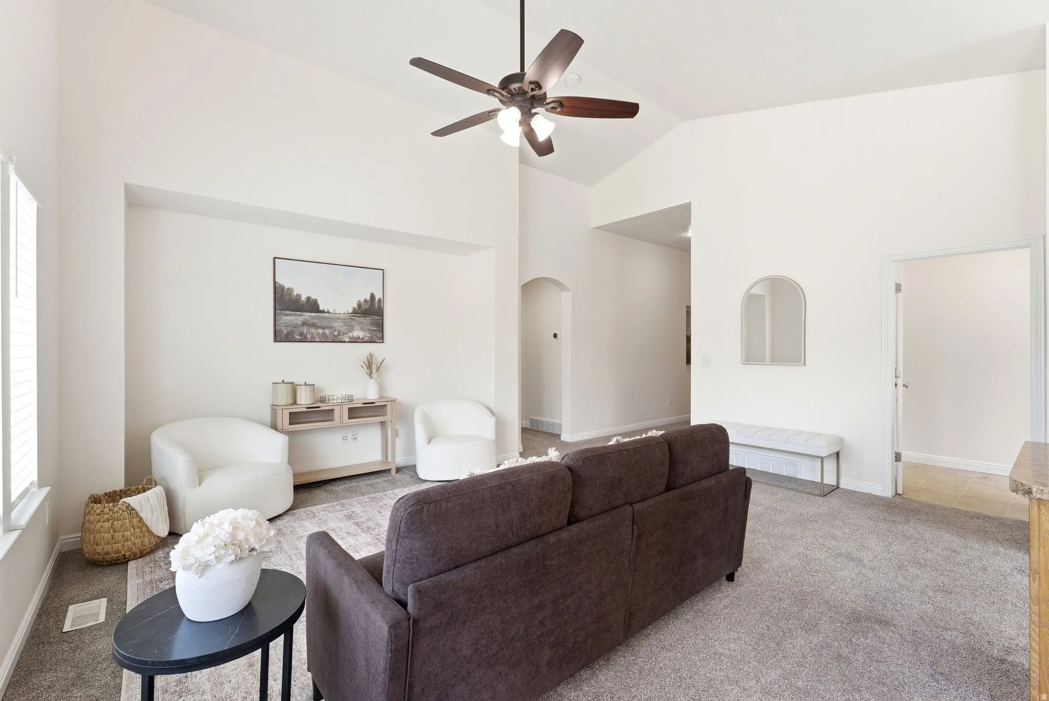 Living area with light colored carpet, a ceiling fan, arched walkways, and lofted ceiling
