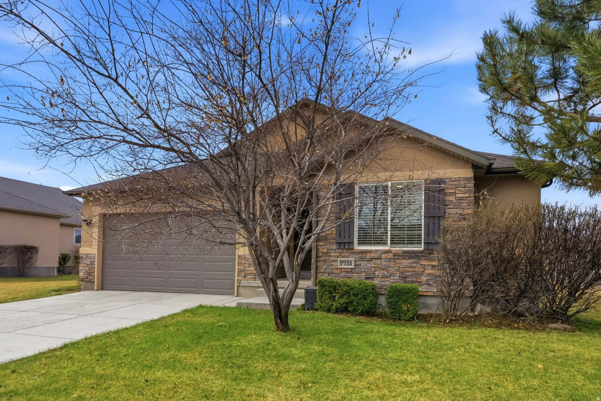 View of front of property with stone siding, concrete driveway, a front yard, an attached garage, and stucco siding