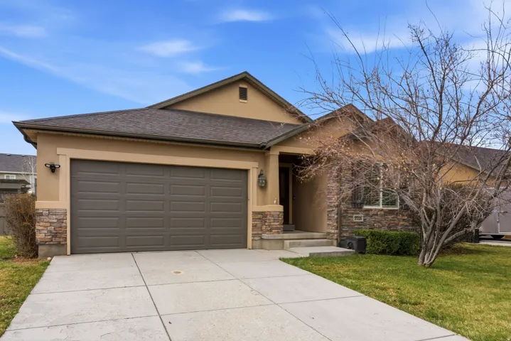 View of front of property featuring stone siding, an attached garage, stucco siding, concrete driveway, and a front lawn