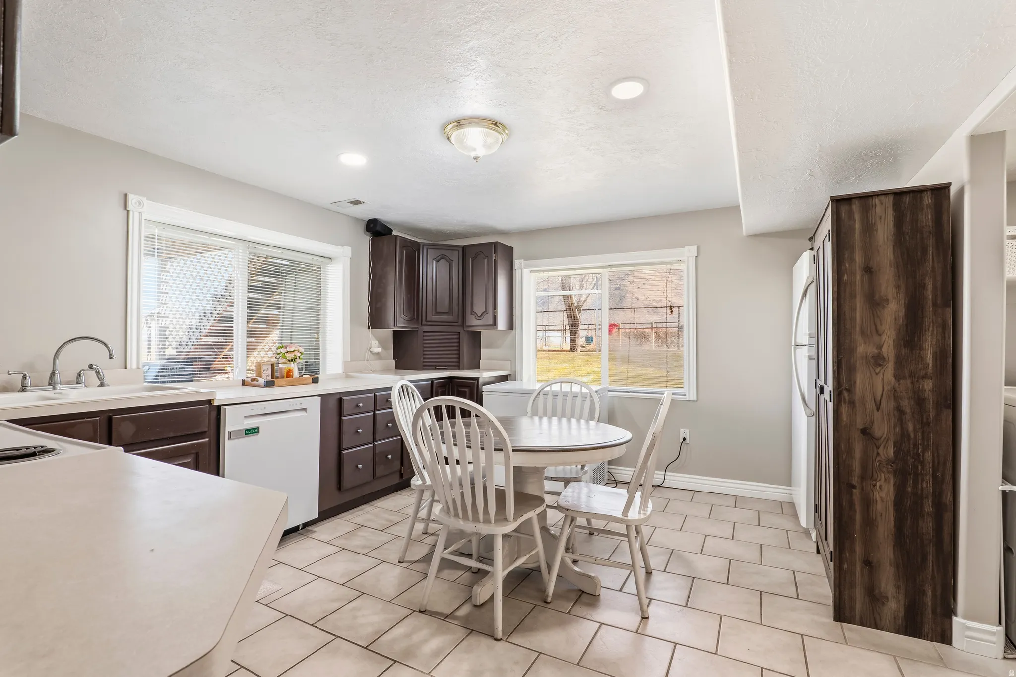 Kitchen with dark wood finish cabinetry, light countertops, white appliances, recessed lighting, and light tile patterned floors