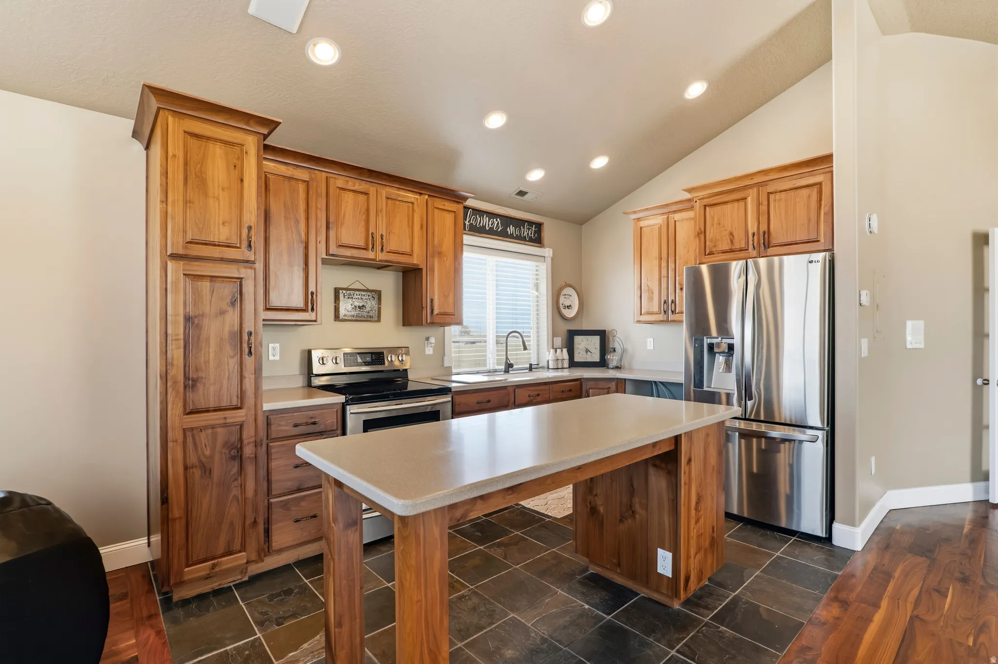 Kitchen featuring stainless steel appliances, lofted ceiling, light countertops, wood finish cabinets, and a center island