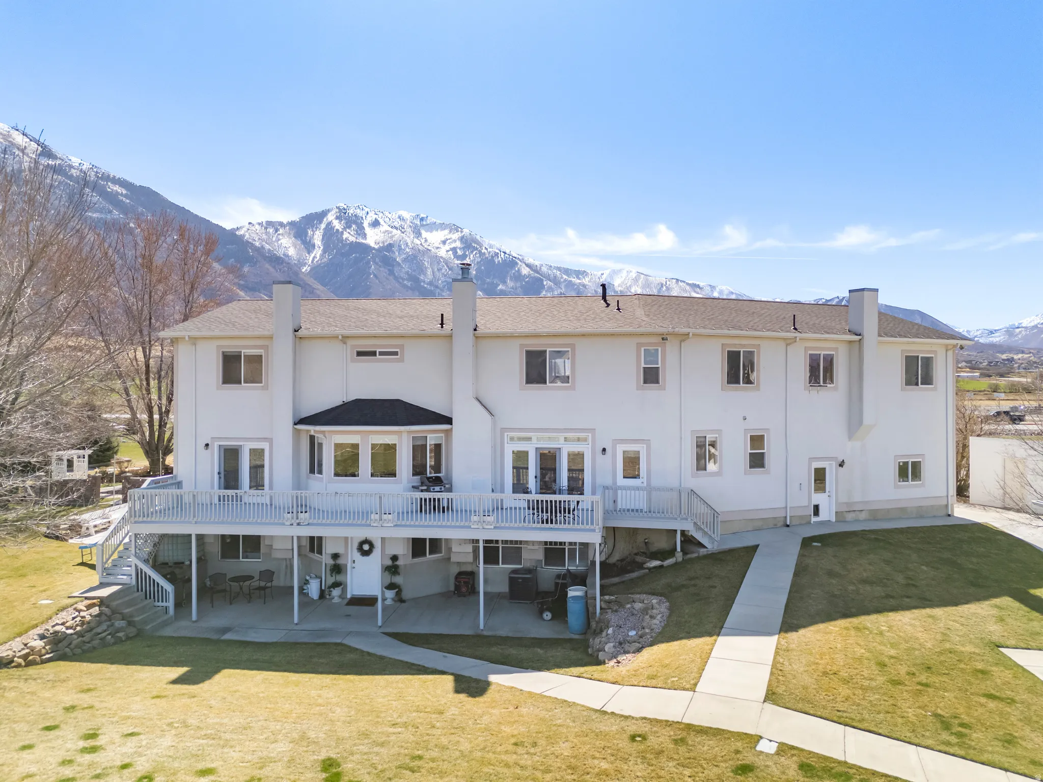 Rear view of house with a yard, a patio, a chimney, a deck with mountain view, and stucco siding