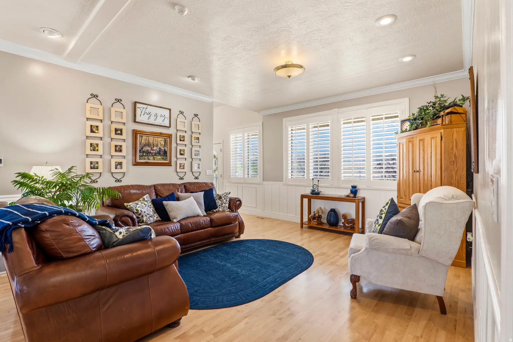 Living area featuring wainscoting, light wood finished floors, crown molding, and a textured ceiling