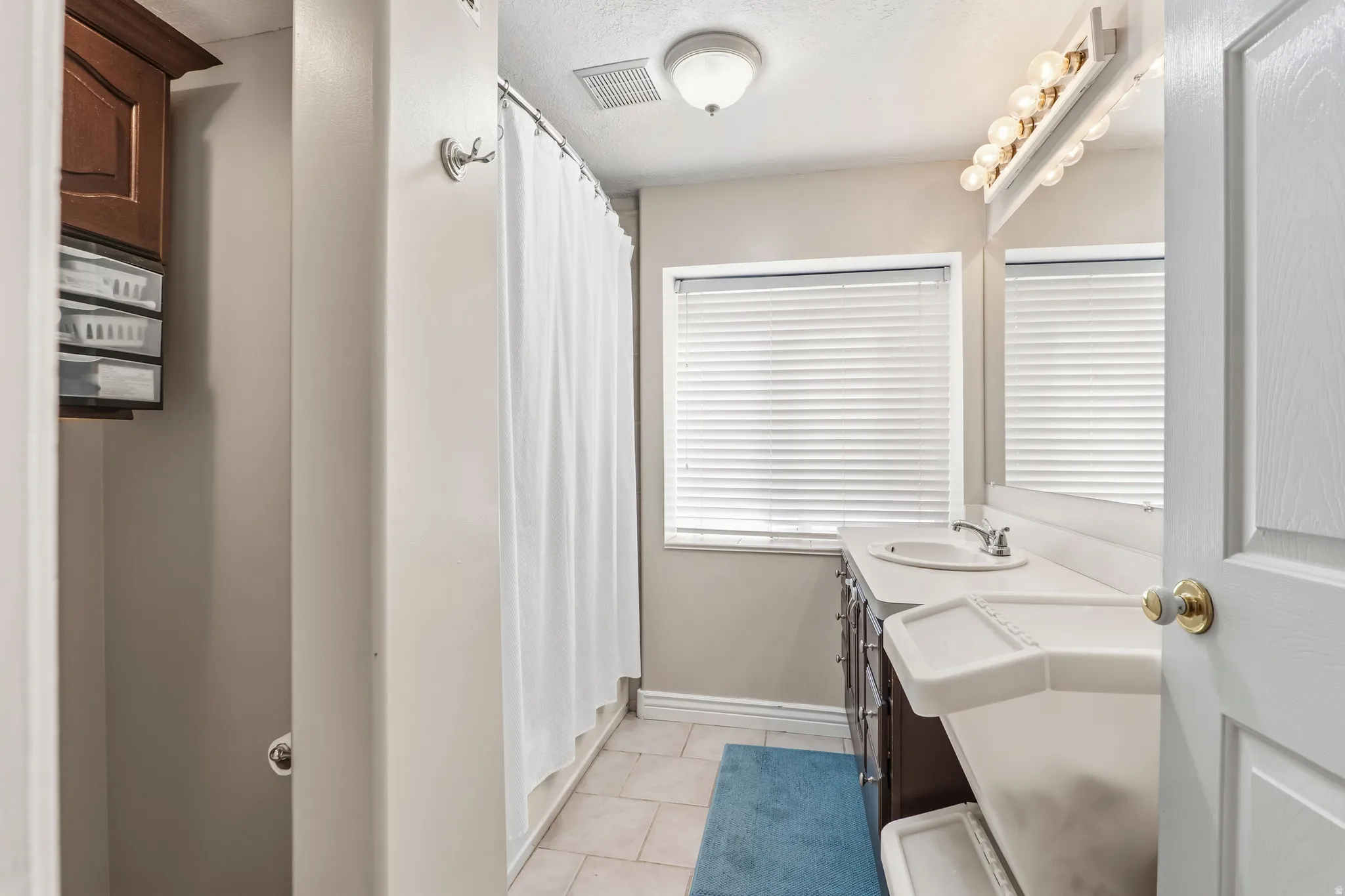 Bathroom with double vanity, a shower with shower curtain, light tile patterned flooring, and a textured ceiling