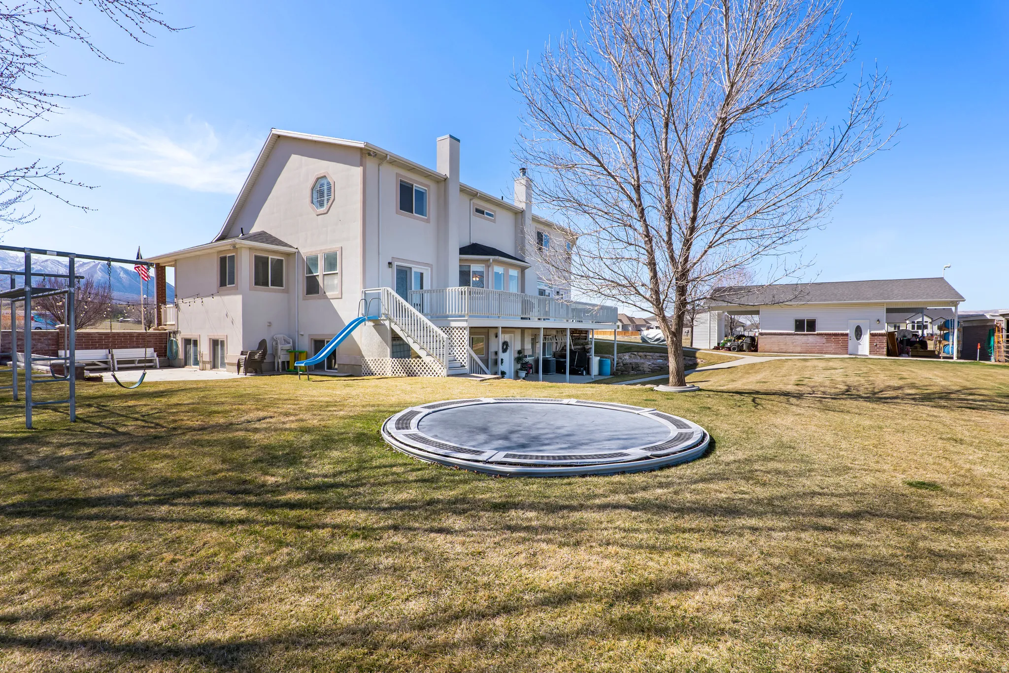 Back of property with a trampoline, a patio area, a chimney, a lawn, and a wooden deck