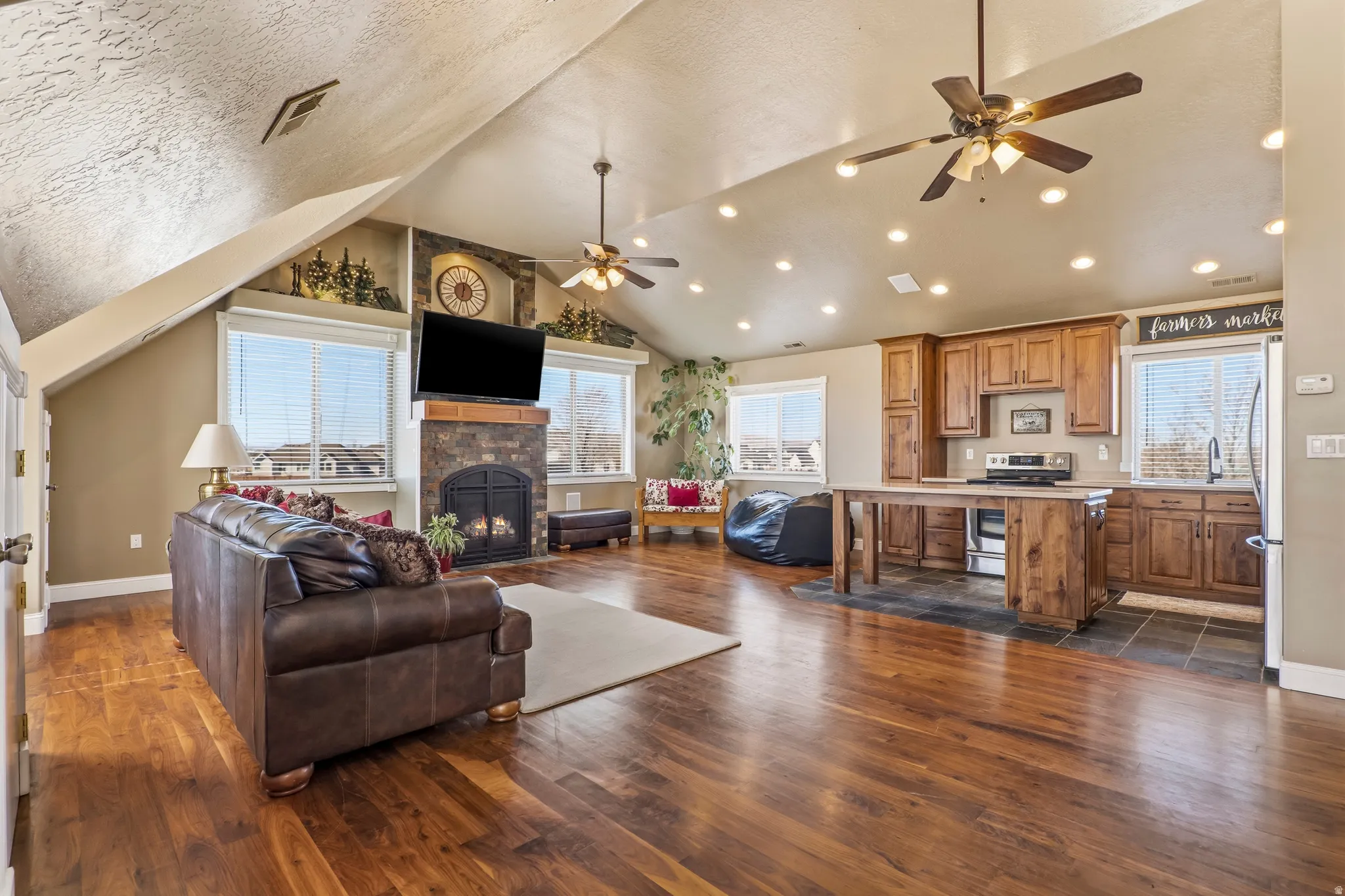 Living room with ceiling fan, dark wood finished floors, a lit fireplace, and plenty of natural light