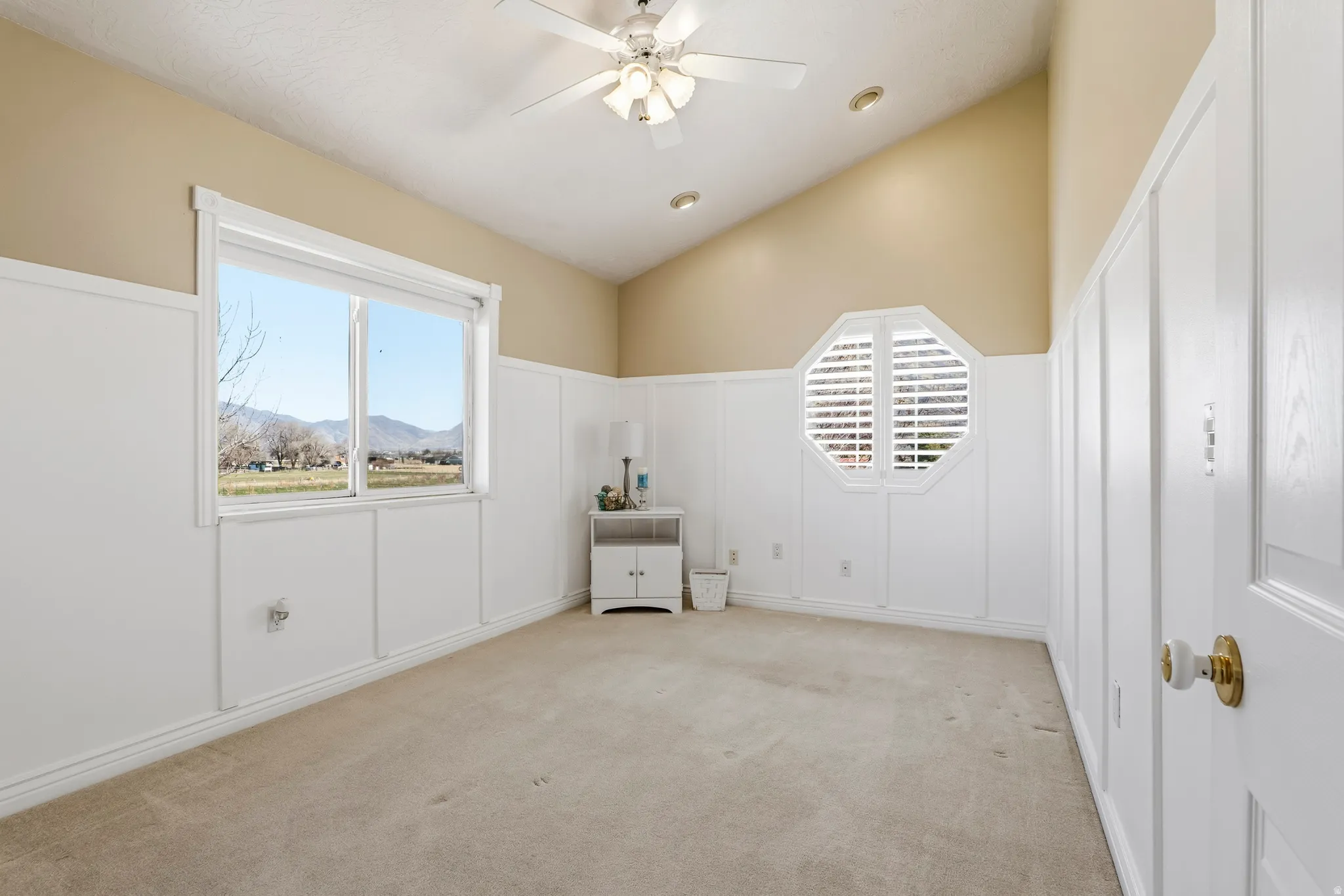 Spare room featuring a decorative wall, a wainscoted wall, vaulted ceiling, a ceiling fan, and light carpet