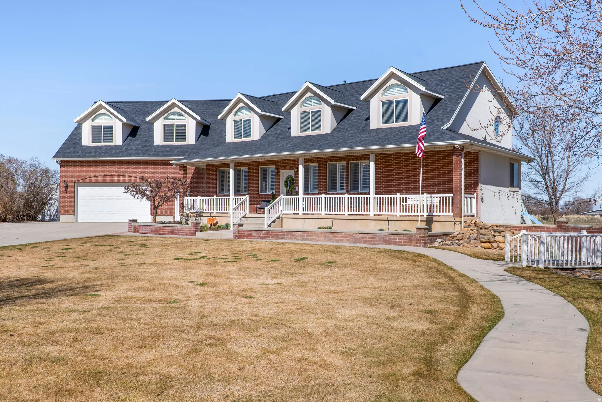Cape cod house featuring brick siding, covered porch, a garage, and concrete driveway
