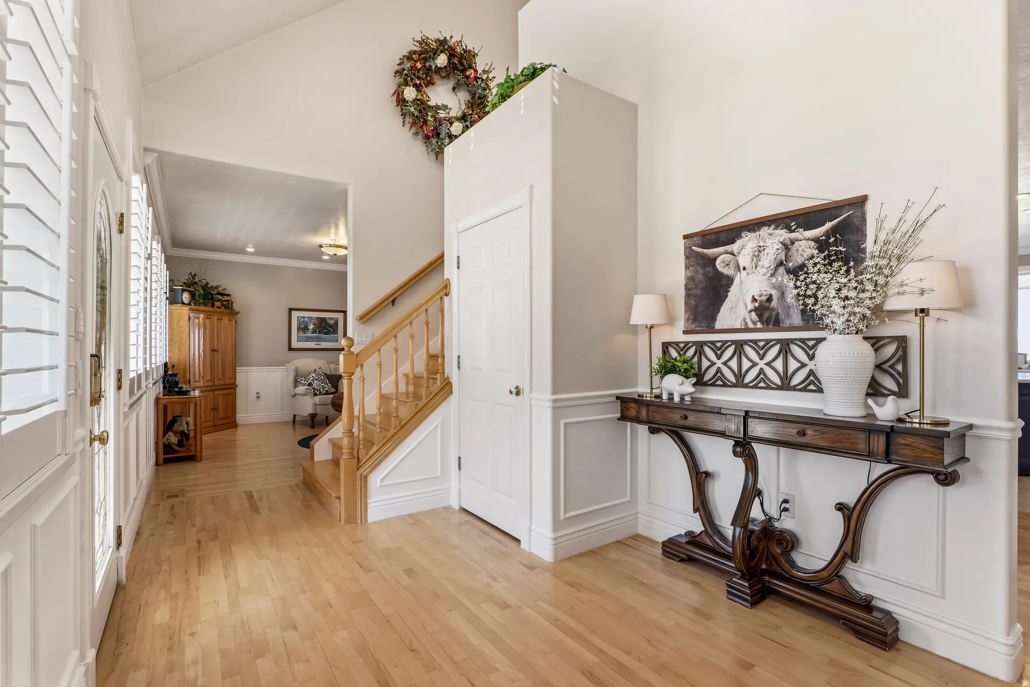 Foyer with wainscoting, light wood-style floors, a decorative wall, a high ceiling, and crown molding