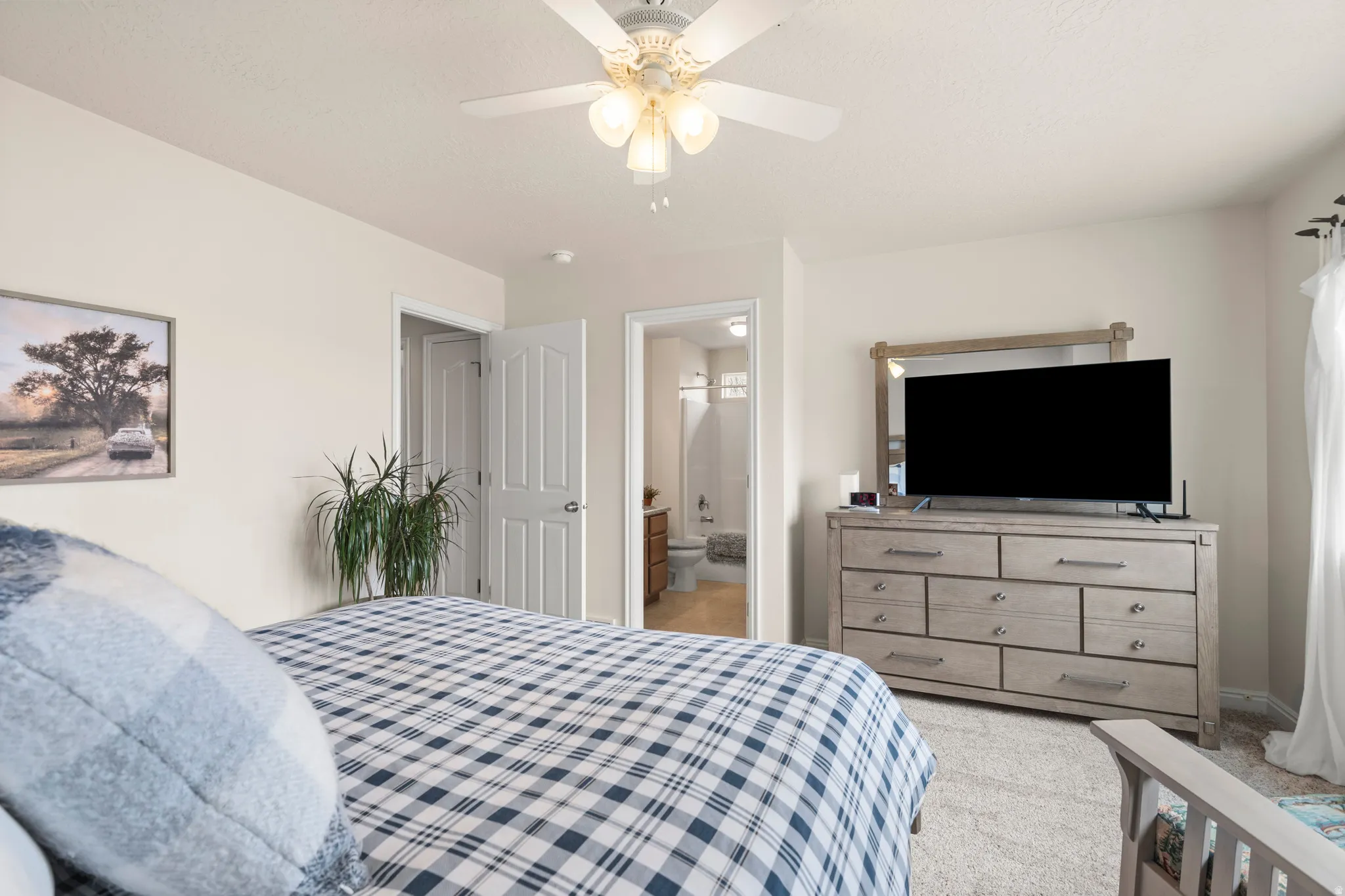 Bedroom with light carpet, ceiling fan, and ensuite bathroom