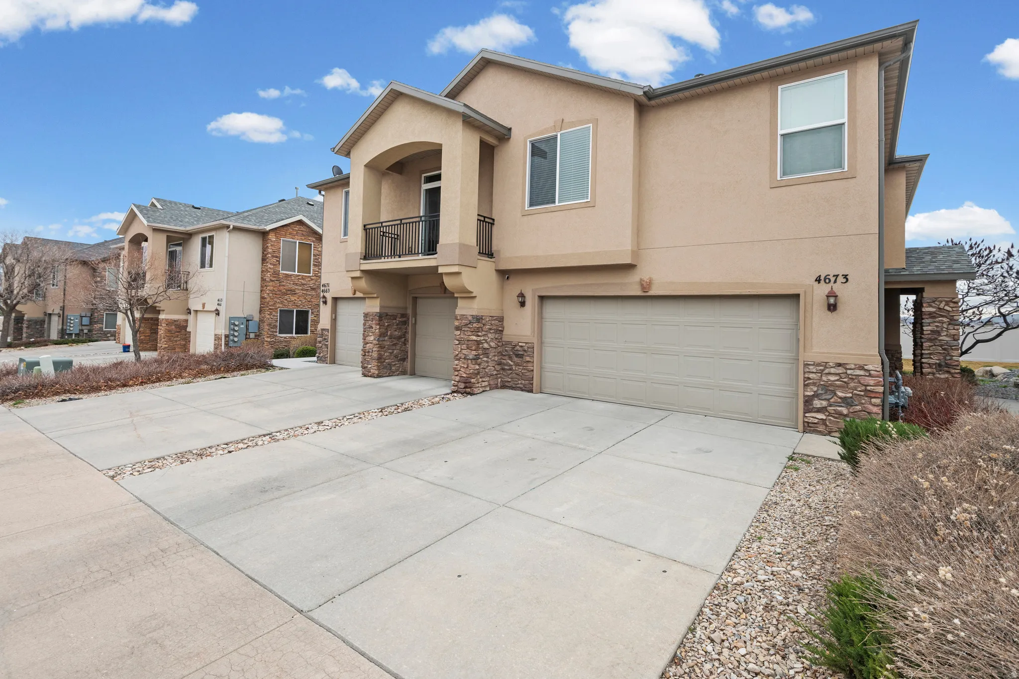 Traditional-style house with stone siding, a balcony, an attached garage, driveway, and stucco siding